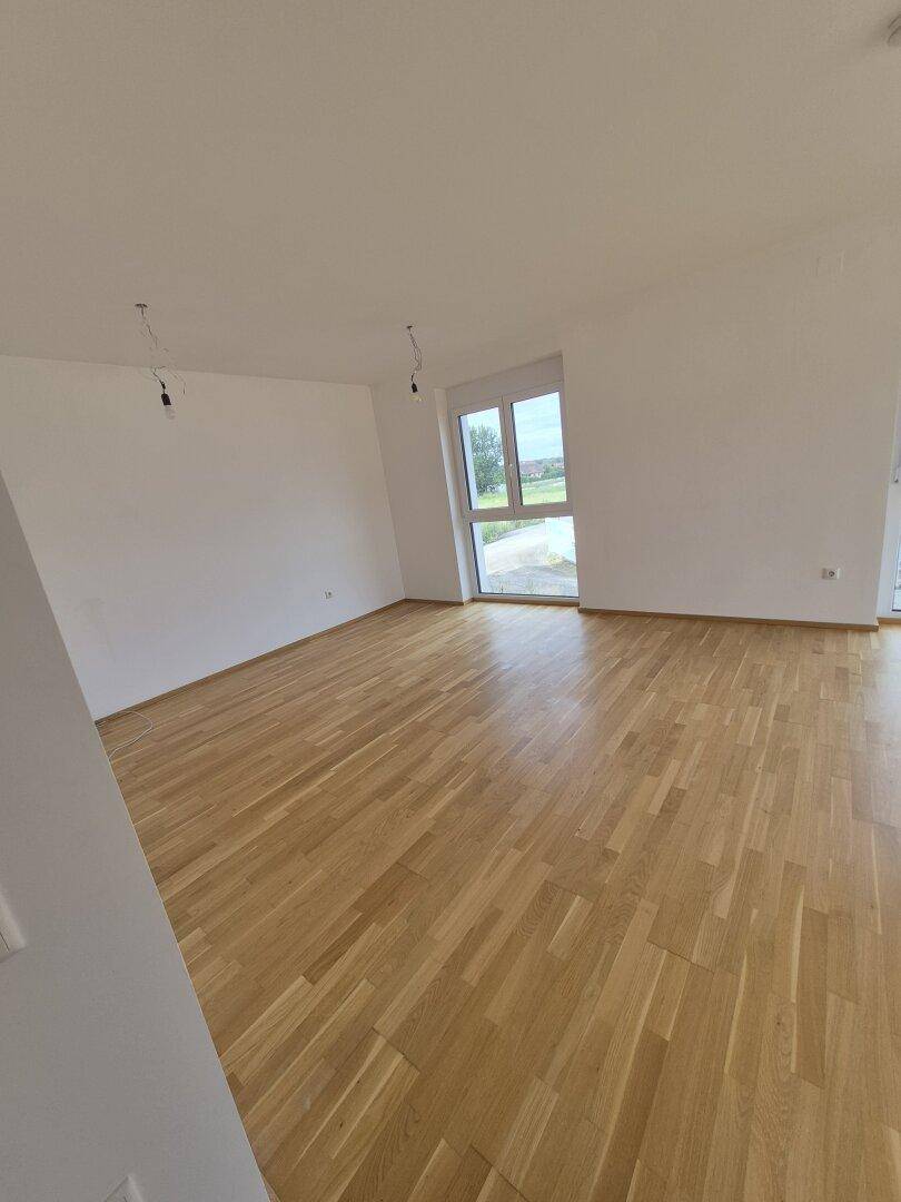 Heller Wohnraum mit Parkettboden und großem Fenster, das viel Tageslicht hereinlässt.