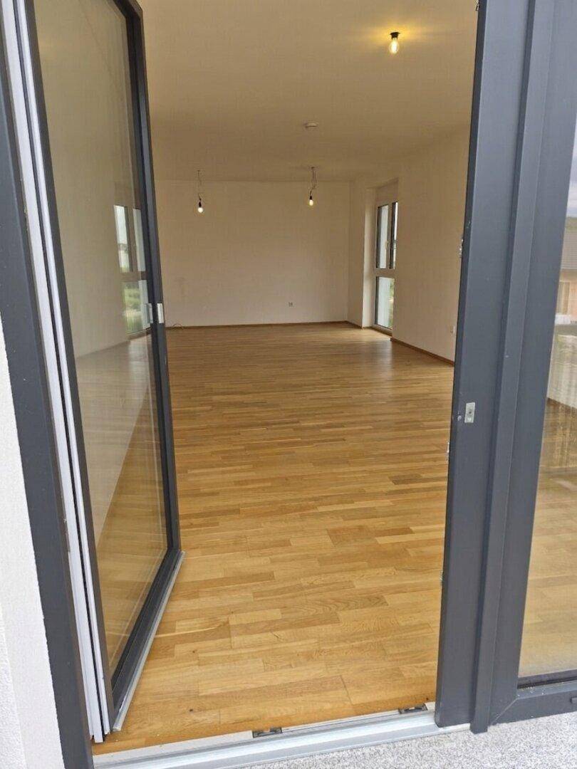Offene Balkontür führt in einen hellen, unmöblierten Raum mit Parkettboden.