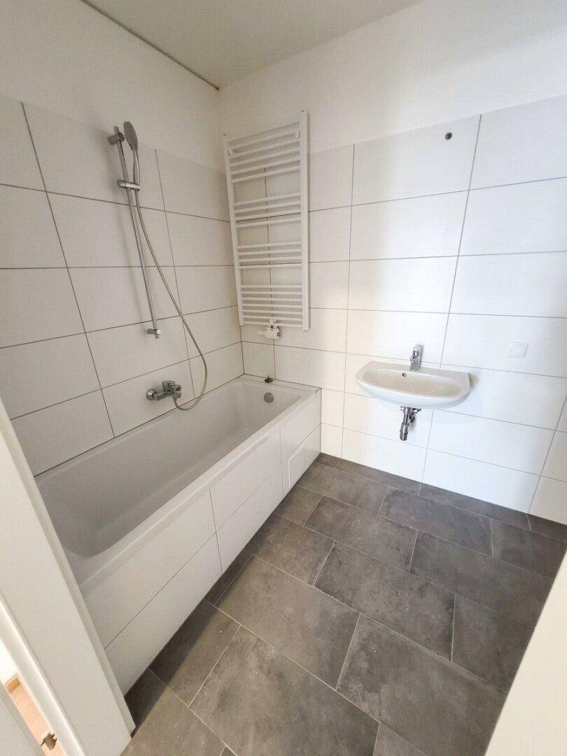 Modernes Badezimmer mit Badewanne, Dusche, Waschbecken und dunklen Bodenfliesen.