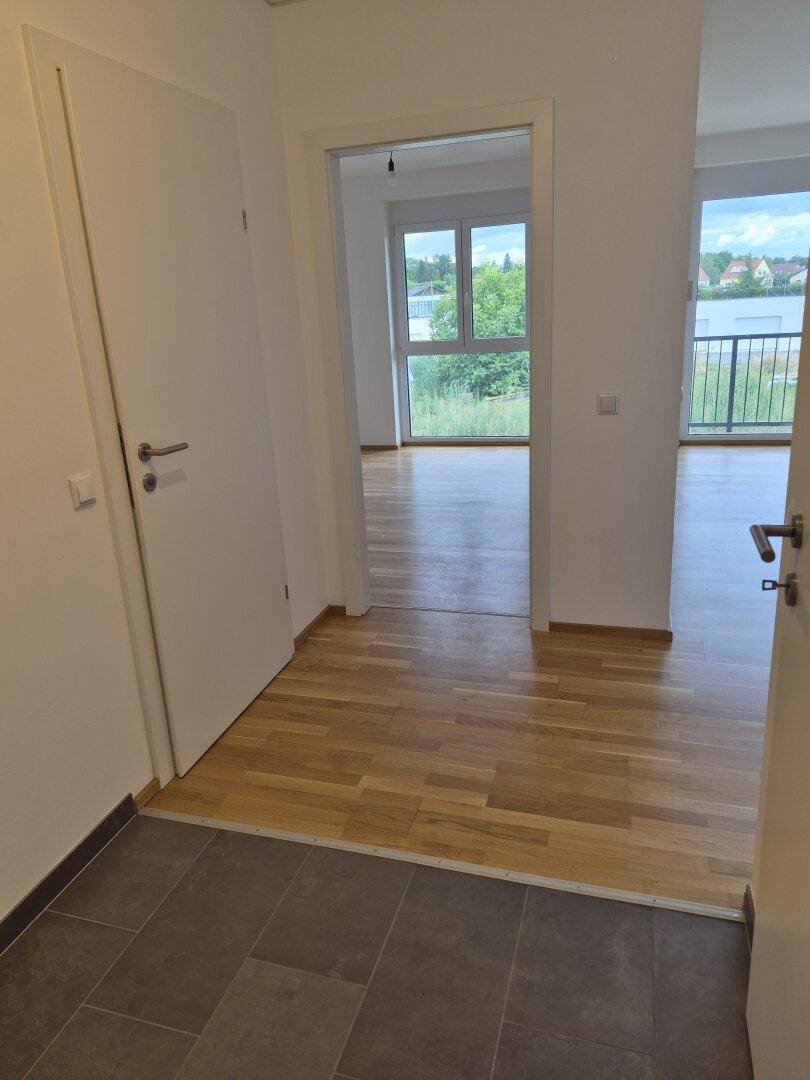Heller Flur mit Fliesenboden, der in einen Wohnbereich mit Parkett und großen Fenstern übergeht.