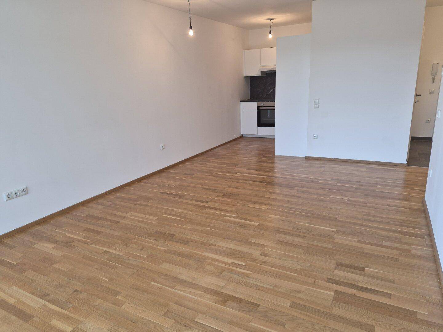 Weitläufiger Wohnbereich mit integrierter Küche und Eichenparkett, ideal für modernes Wohnen.