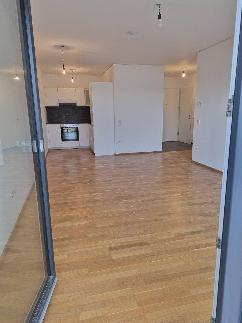 Blick vom Balkon in den hellen Wohnbereich mit Parkettboden und moderner Küchenzeile.