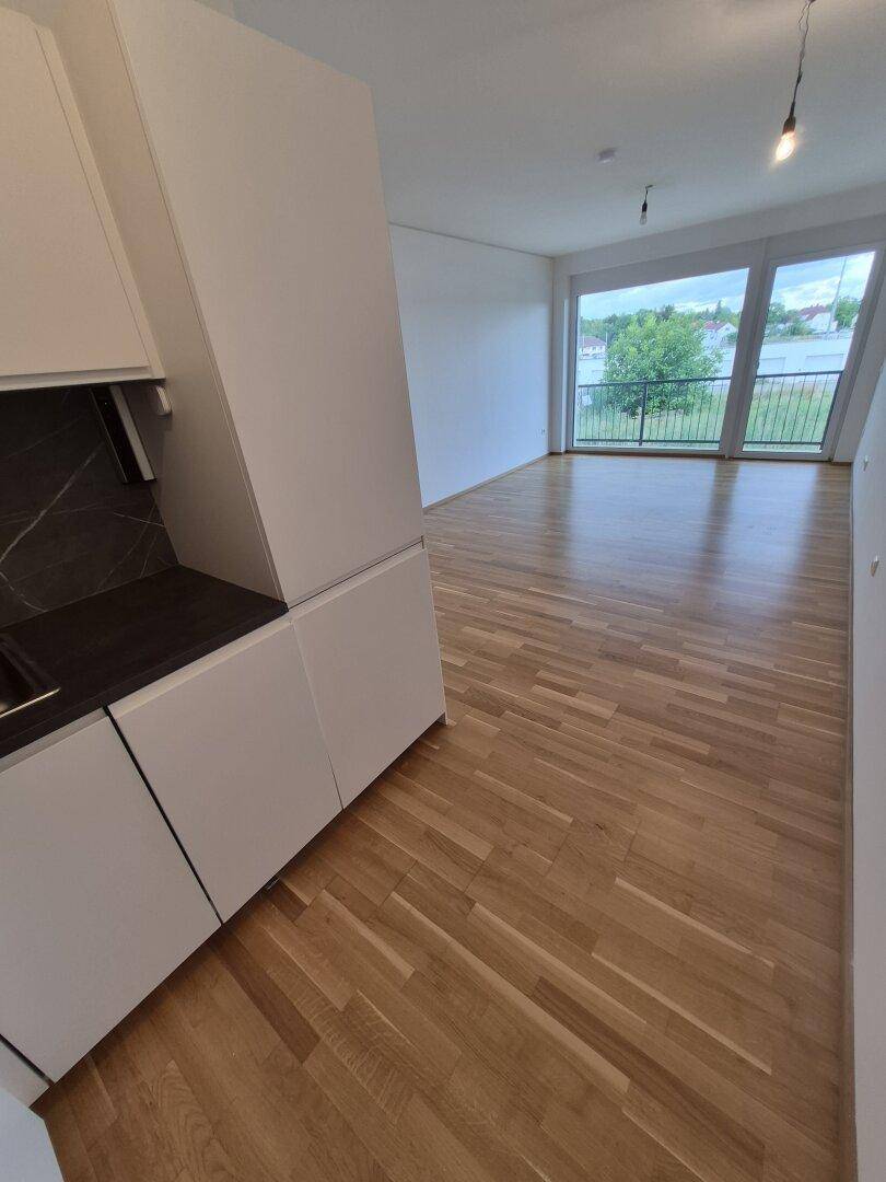 Heller Wohnbereich mit moderner Küchenzeile und großem Fenster, das viel Tageslicht hereinlässt.