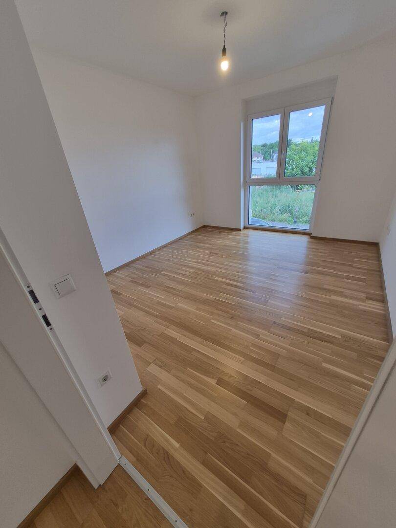 Leeres Schlafzimmer mit hellem Parkettboden und großem Fenster, das einen weiten Ausblick bietet.