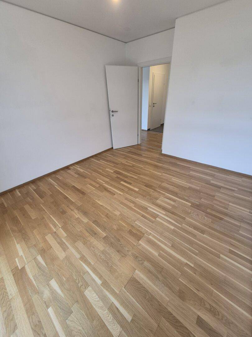 Helles Schlafzimmer mit Parkettboden und weiß gestrichenen Wänden, bereit zur individuellen Gestaltung.