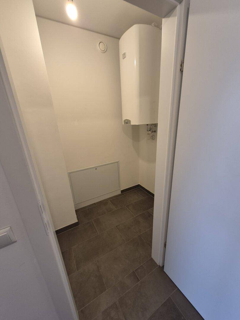 Praktischer Hauswirtschaftsraum mit Warmwasserbereiter und pflegeleichtem Fliesenboden.