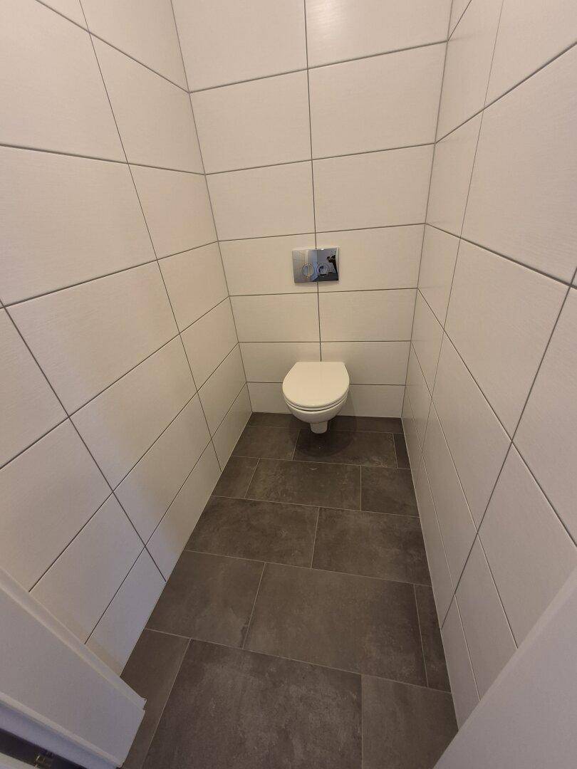 Separates WC mit wandhängender Toilette und modernen Fliesen an Wänden und Boden.