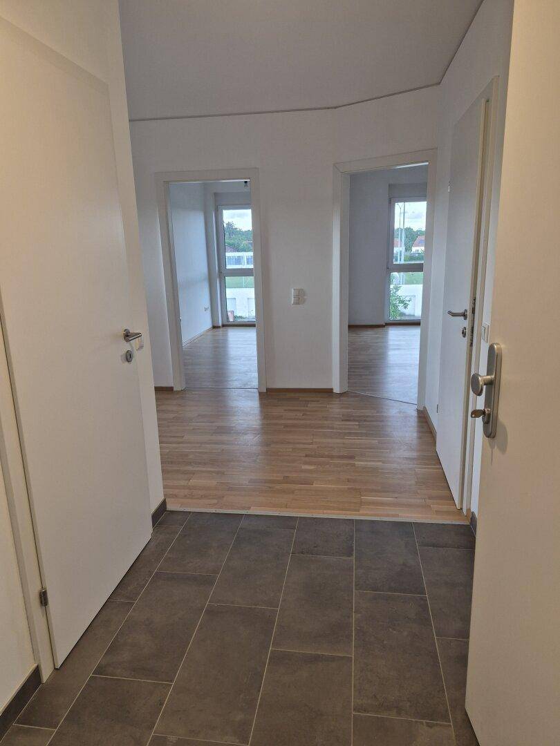 Heller Eingangsbereich mit Fliesenboden, der zu Zimmern mit Parkettboden führt.