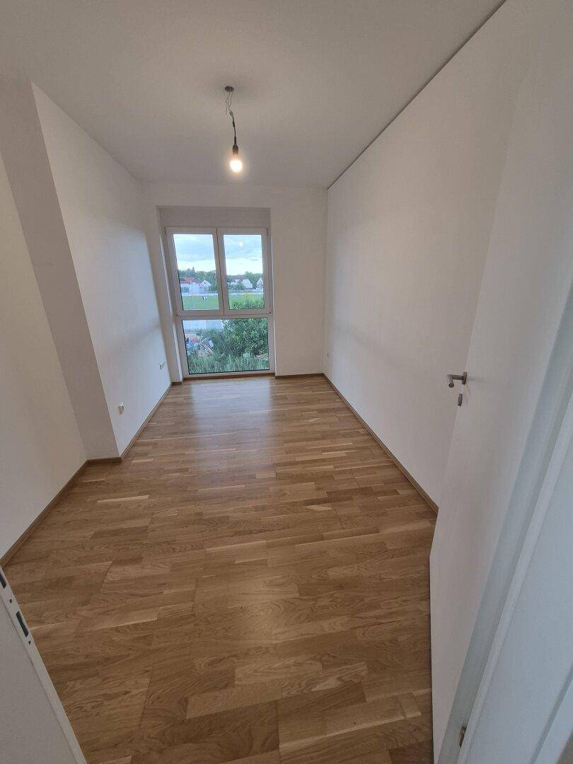 Helles, leeres Zimmer mit Parkettboden und Fenster, das einen weiten Blick ermöglicht.
