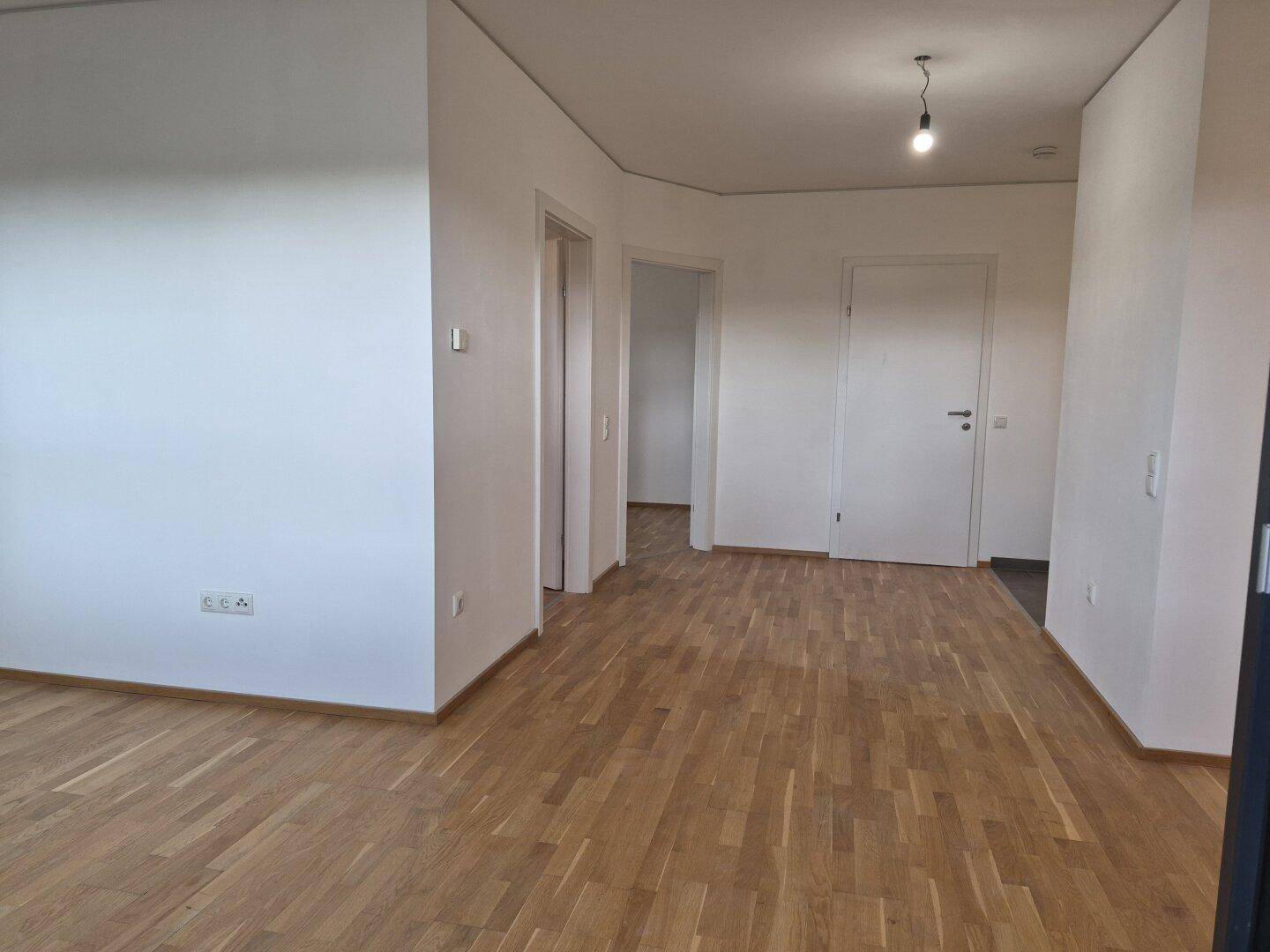 Geräumiger Wohnbereich mit Parkettboden und weiß gestrichenen Wänden, bietet viel Gestaltungspotenzial.