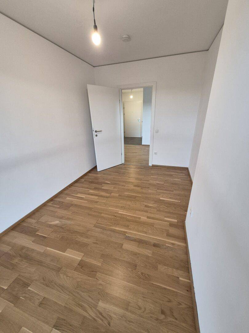 Leeres Zimmer mit Parkettboden und weiß gestrichenen Wänden, bereit zur individuellen Gestaltung.