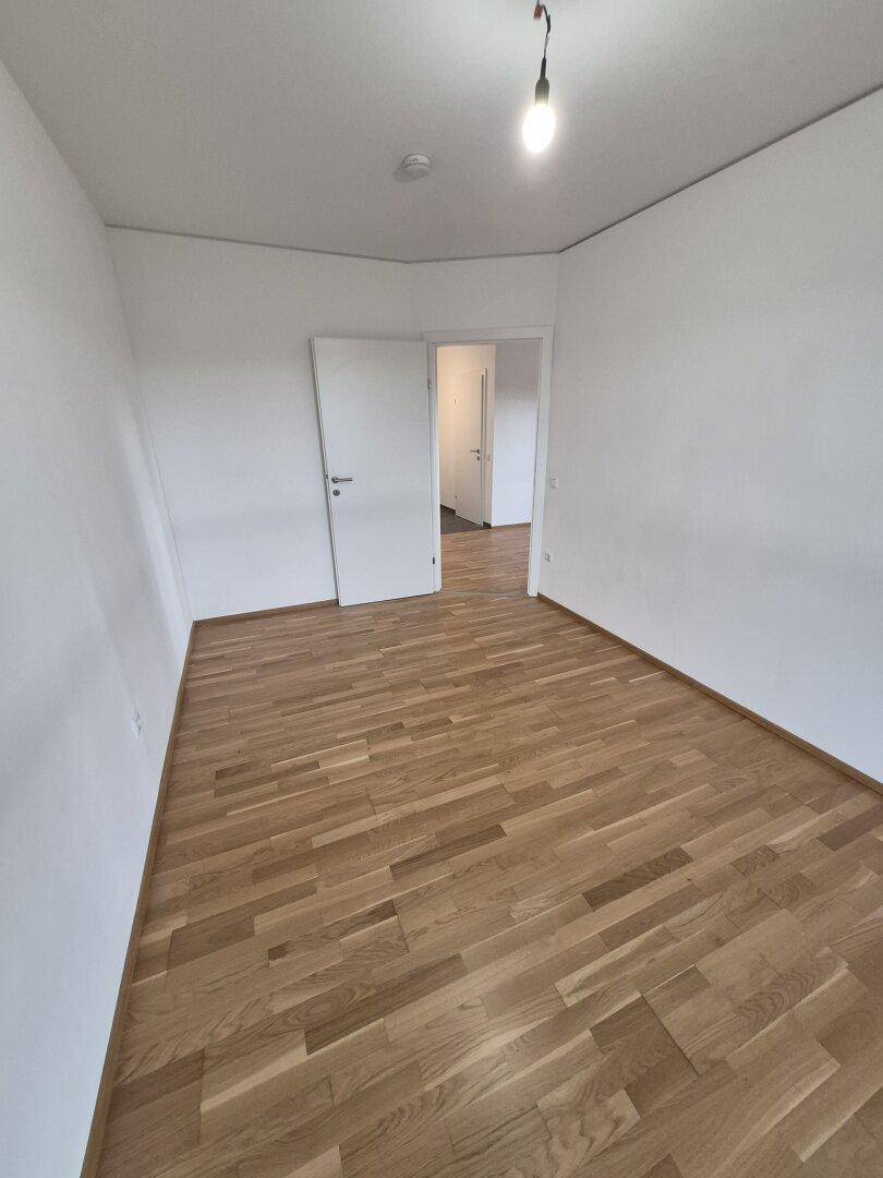 Helles, leeres Zimmer mit Parkettboden und weiß gestrichenen Wänden, ideal für Schlaf- oder Arbeitszimmer.