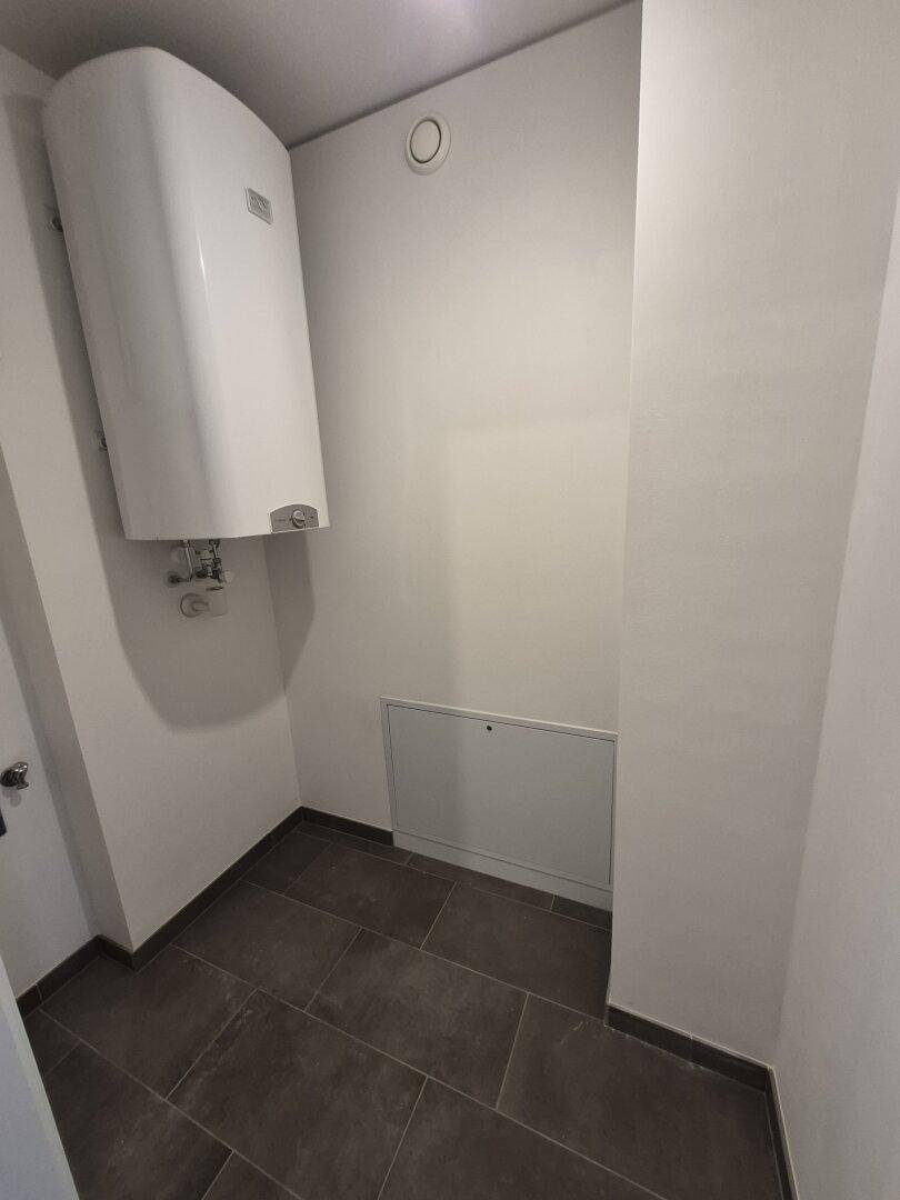 Kleiner Hauswirtschaftsraum mit Warmwasserbereiter und Fliesenboden, praktisch und funktional.