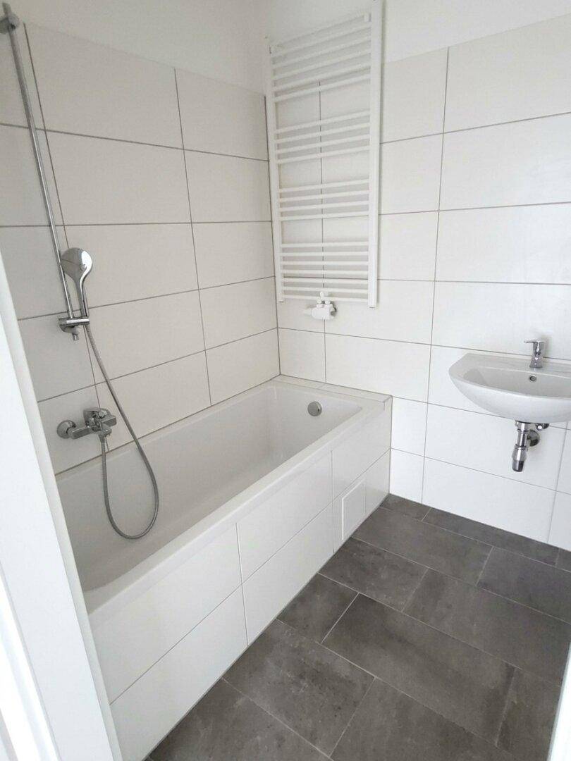 Modernes Badezimmer mit Badewanne, Dusche und Waschbecken, hell gefliest und funktional.