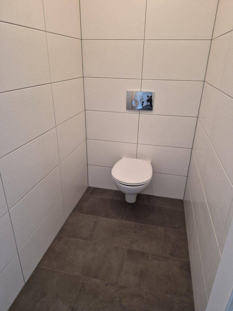 Separates WC mit wandhängender Toilette und modernen Fliesen, sauber und funktional.