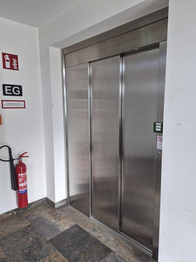 Moderner Aufzug im Eingangsbereich eines Mehrfamilienhauses, mit Fliesenboden und Brandschutz.