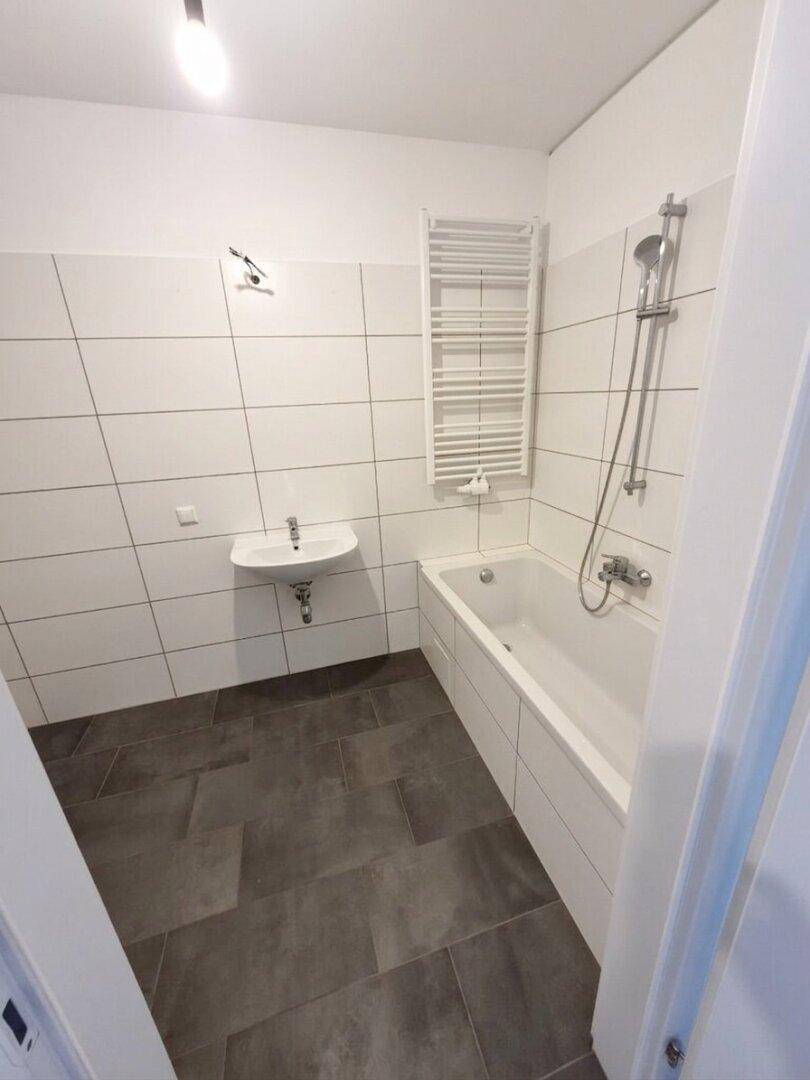 Modernes Badezimmer mit Badewanne, Waschbecken und beheiztem Handtuchhalter, komplett gefliest.