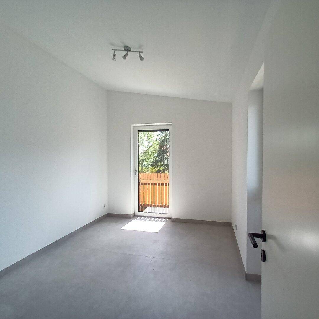Schlafzimmer mit Balkonzugang und schrägen Decken, bietet viel Tageslicht.