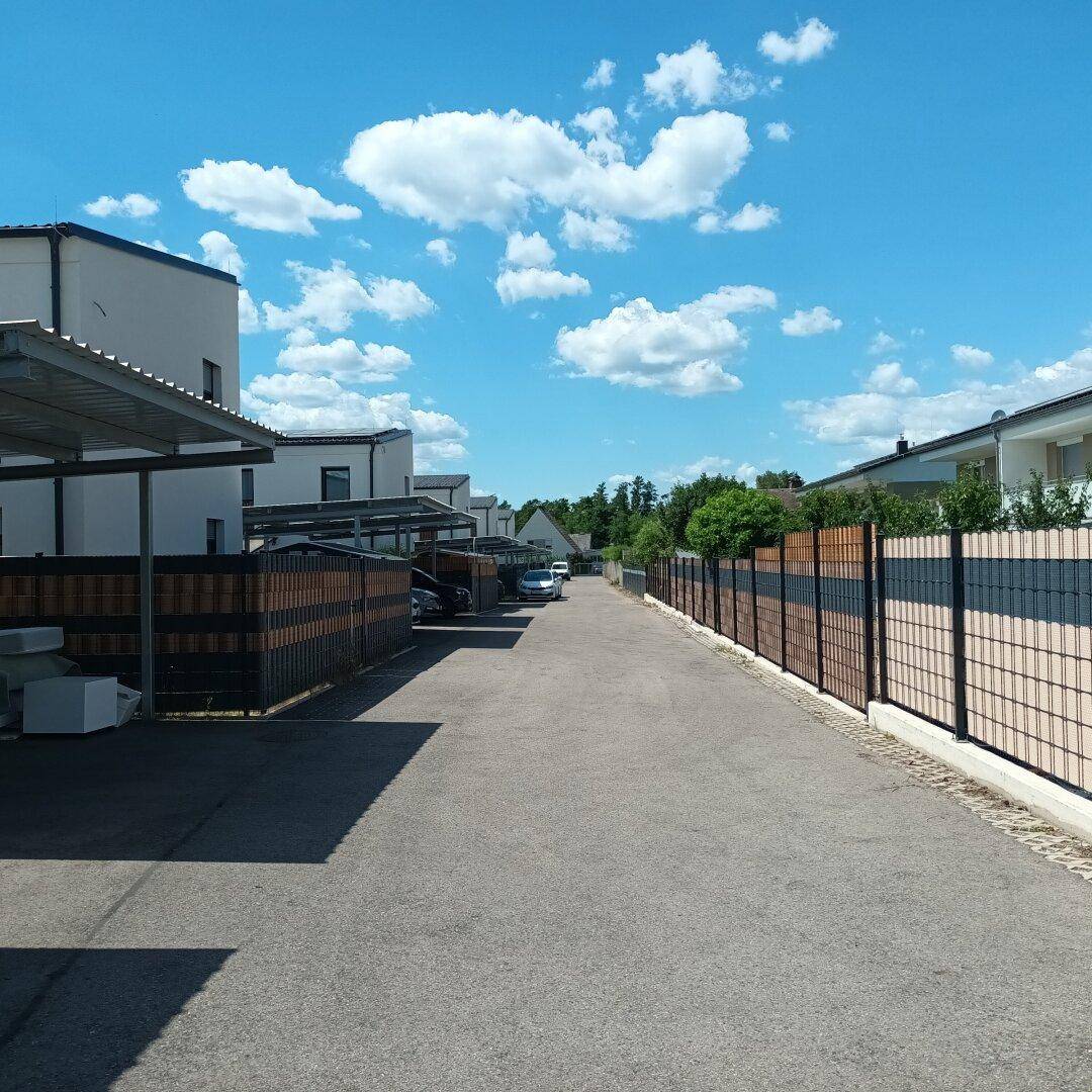 Zufahrtsstraße mit Carports und modernen Häusern in einer Wohnsiedlung.