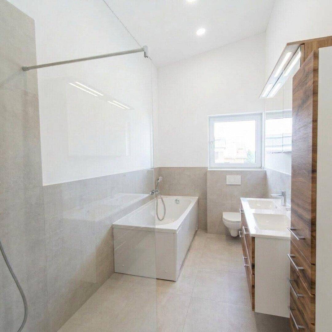 Modernes Badezimmer mit Badewanne, Dusche und Doppelwaschbecken in Holzoptik.