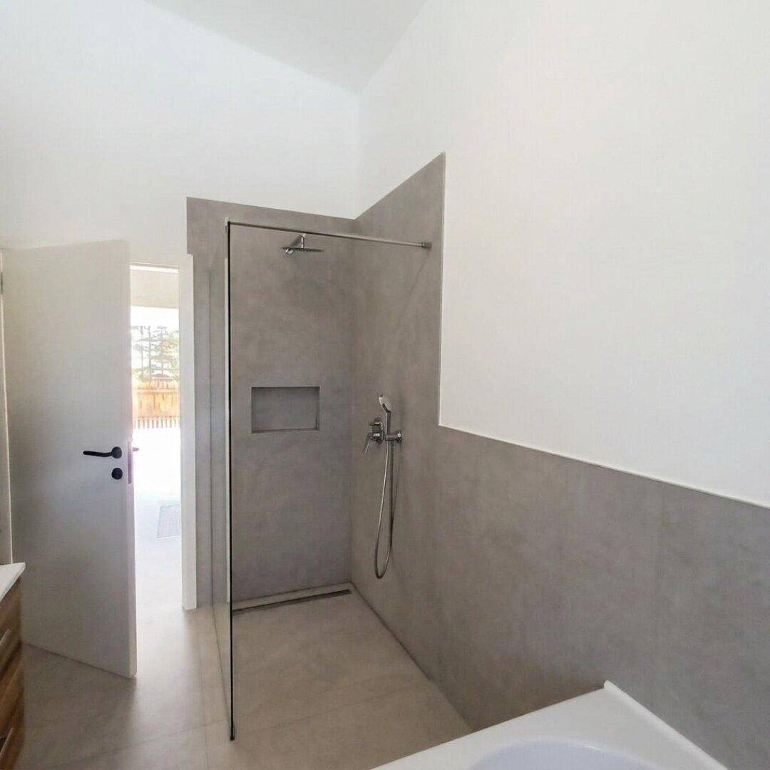 Geräumige, ebenerdige Dusche mit Glasabtrennung und modernen grauen Fliesen.