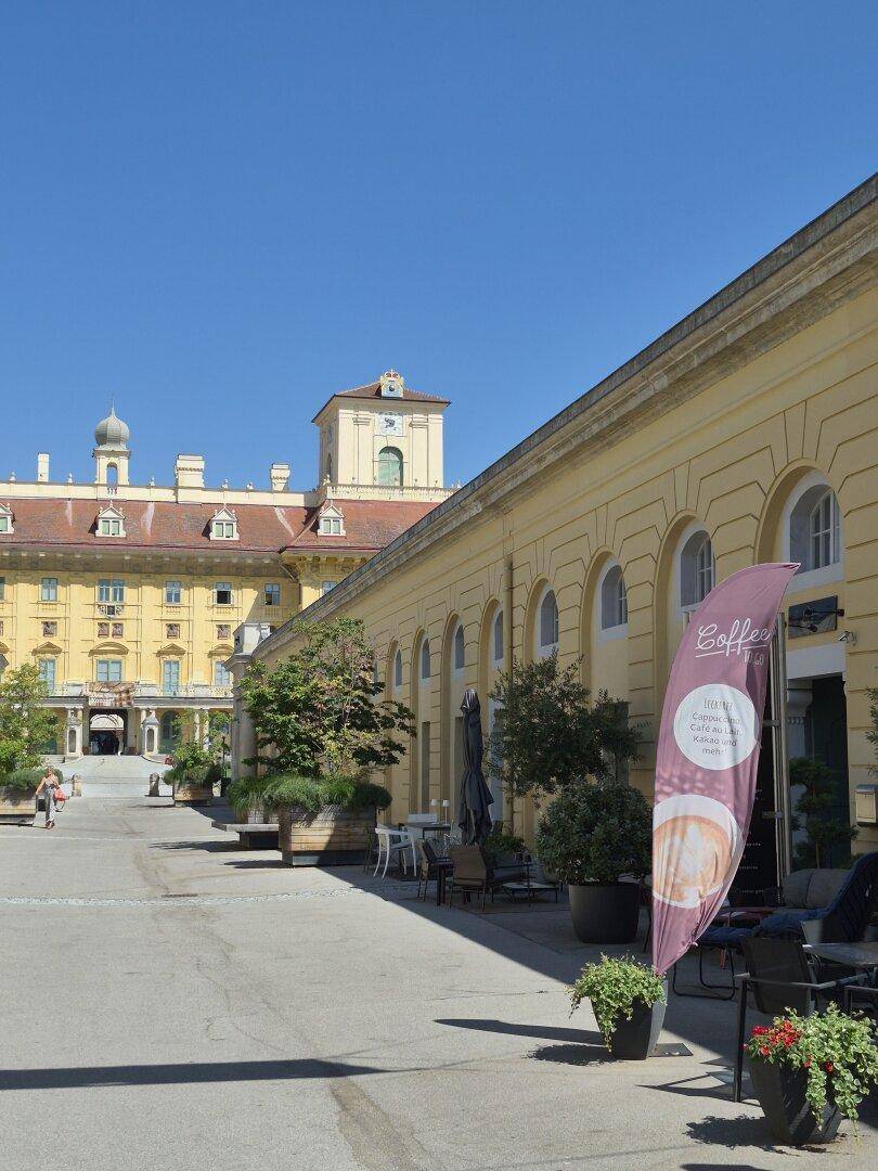 Historisches Gebäude mit Arkaden und einem Café im Freien an einem sonnigen Tag, belebt und charmant.