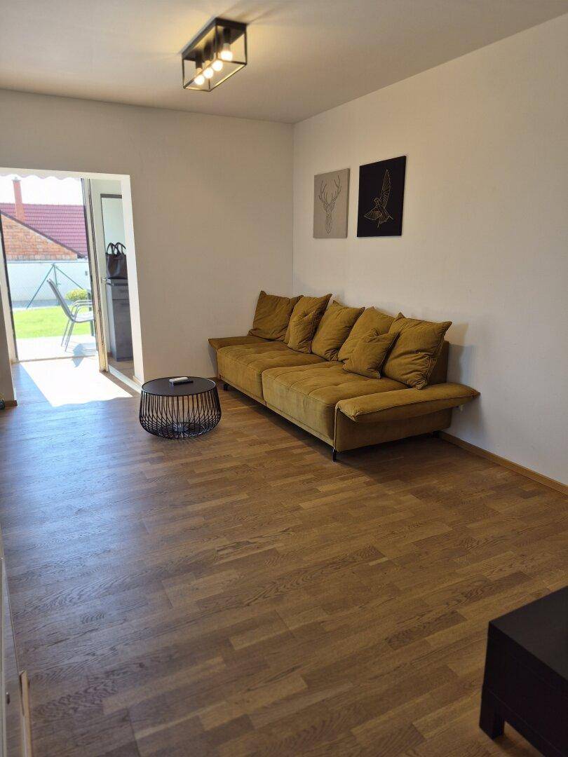 Gemütliches Wohnzimmer mit beiger Couch, Holzboden und Zugang zur Terrasse.