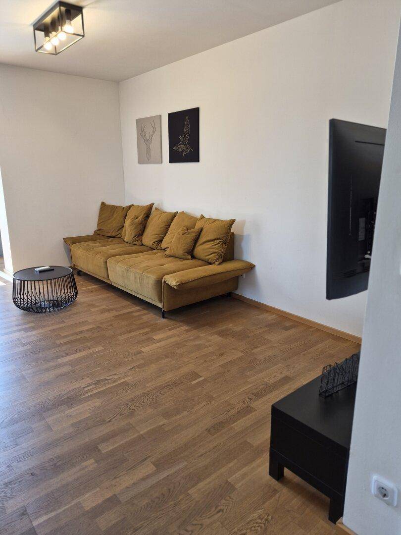 Helles Wohnzimmer mit beiger Couch, Holzboden und Wandfernseher.