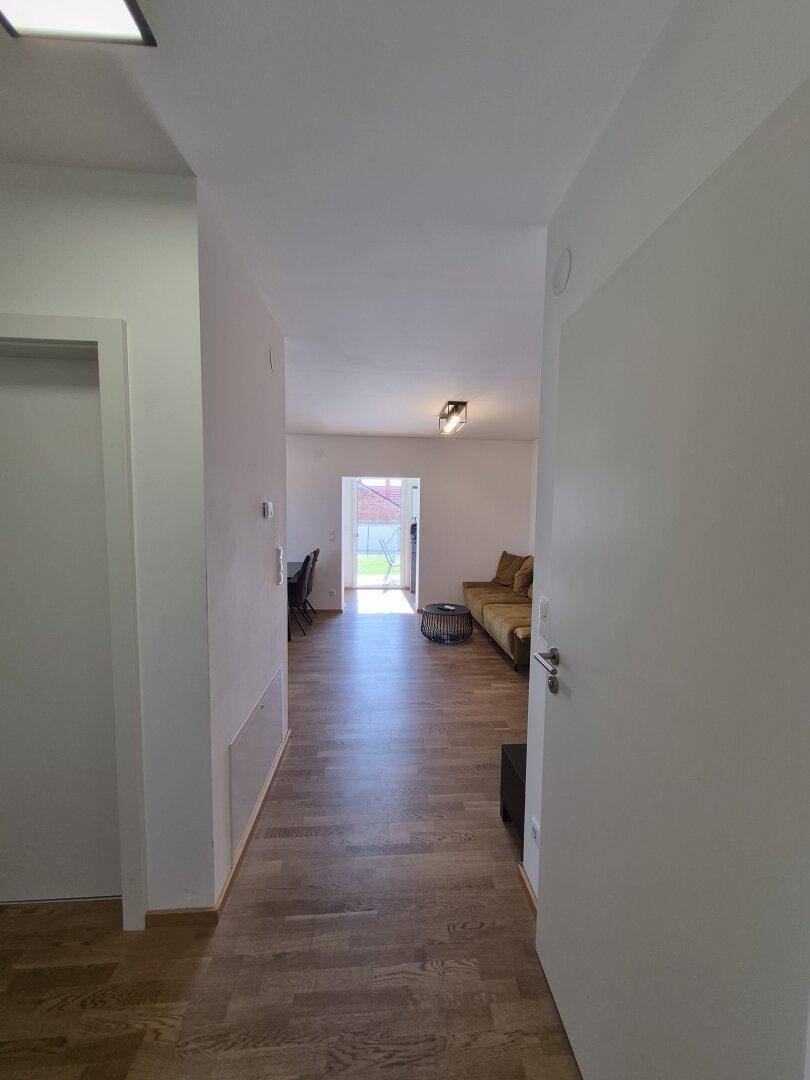 Heller Flur mit Holzboden, der in einen offenen Wohnbereich führt.