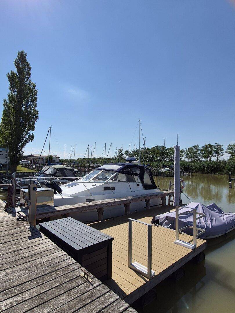 Boote liegen an einem sonnigen Steg in einem Yachthafen mit klarem Himmel.