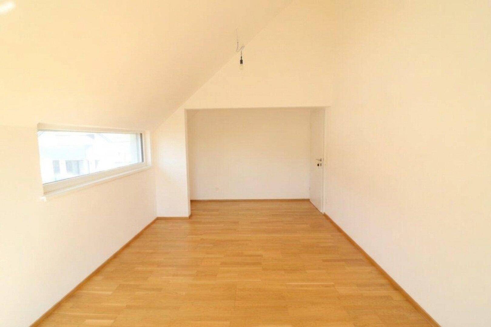 Helles Zimmer im Dachgeschoss mit Holzboden und schrägem Fenster.