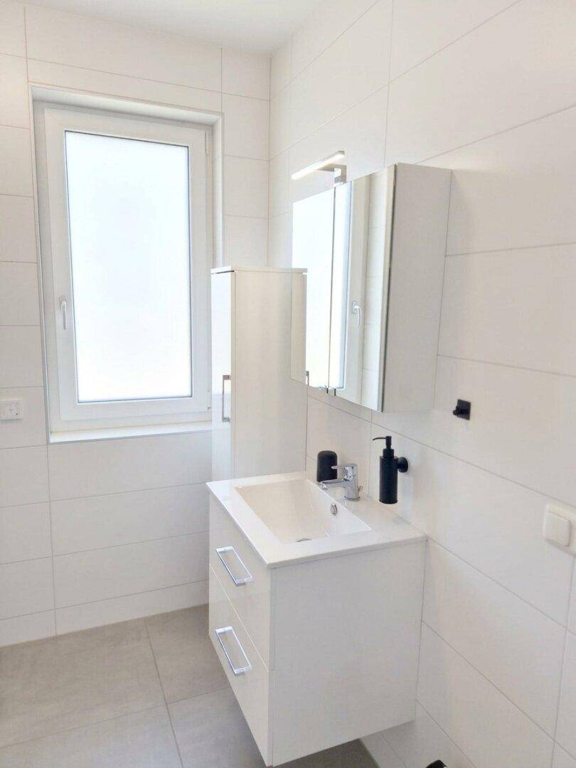 Modernes Badezimmer mit weißen Fliesen, Waschtisch und Fenster.