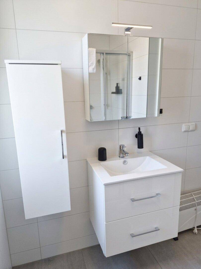 Modernes Badezimmer mit Waschtisch, Spiegelschrank und weißen Fliesen.