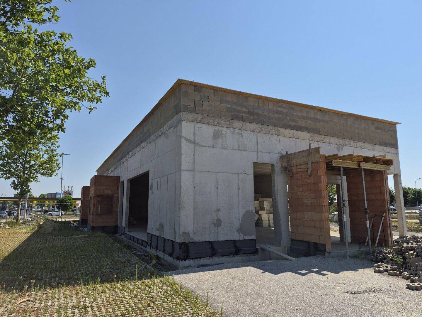 Rückansicht des Rohbaus eines Gewerbegebäudes mit Betonwänden und vorbereiteten Öffnungen für Fenster oder Türen.