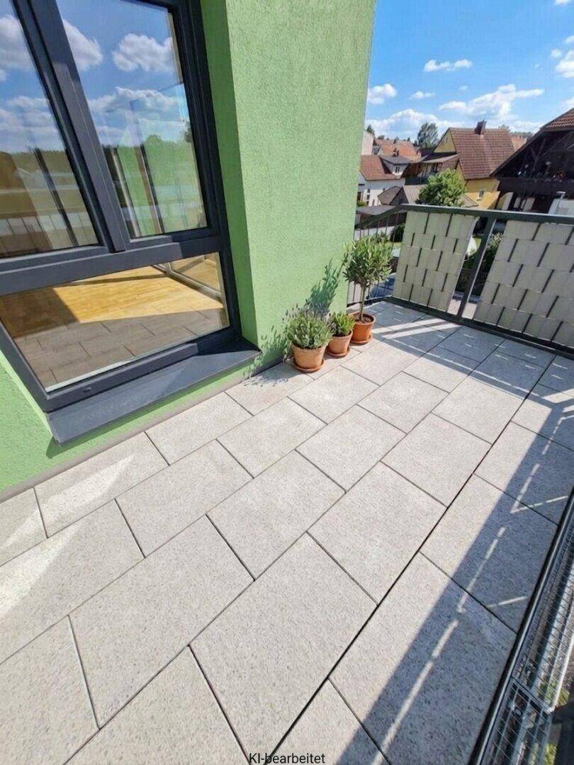 Heller Balkon mit Fliesenboden und Blick auf die umliegende Wohnbebauung und viel Grün.