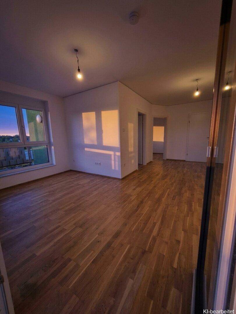 Heller, leerer Raum mit Holzboden und großen Fenstern, die viel Tageslicht hereinlassen.