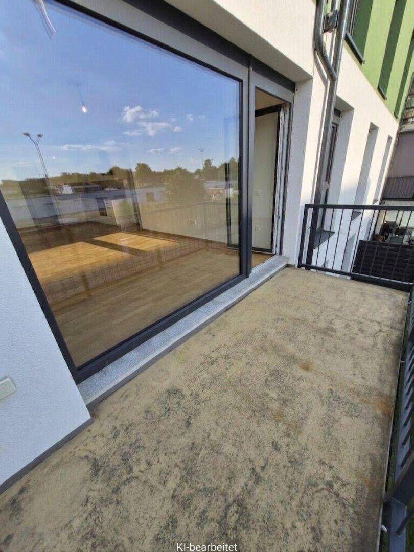 Balkon mit Betonboden und großem Fenster zum hellen Innenraum.