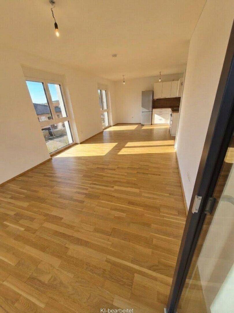 Lichtdurchfluteter, leerer Wohnbereich mit Holzboden und integrierter Küchenzeile.