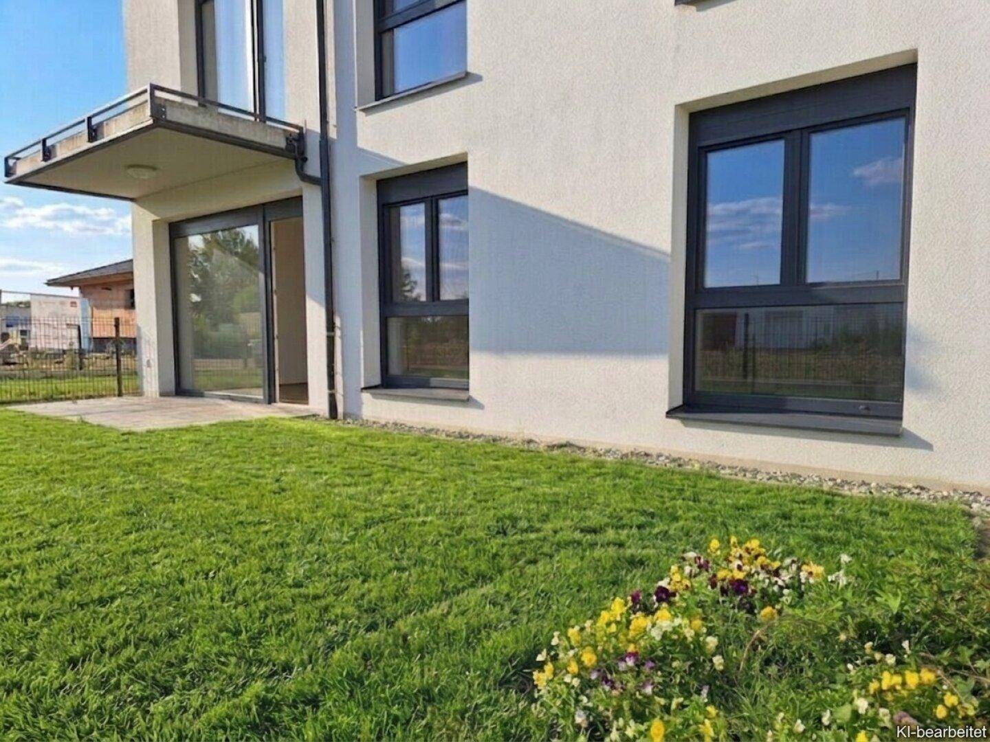Frischer Rasenbereich mit bunten Blumenbeeten vor der modernen Gebäudefassade.