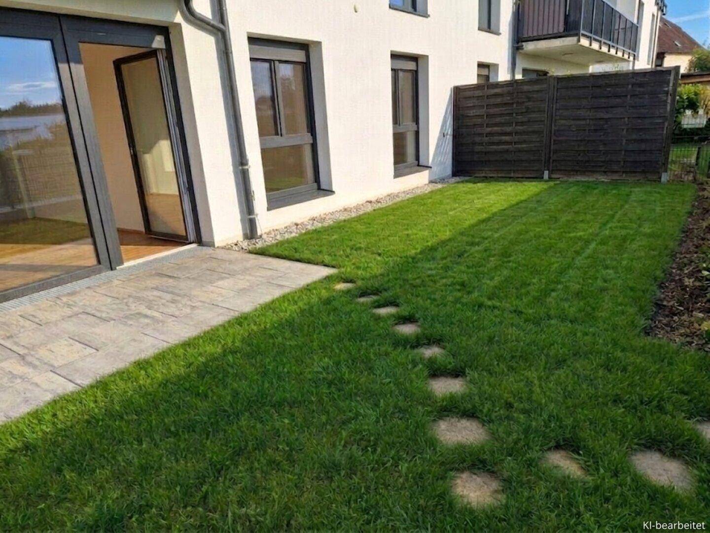 Grüner Rasen mit Trittsteinen und einer gepflasterten Terrasse neben dem Gebäude.
