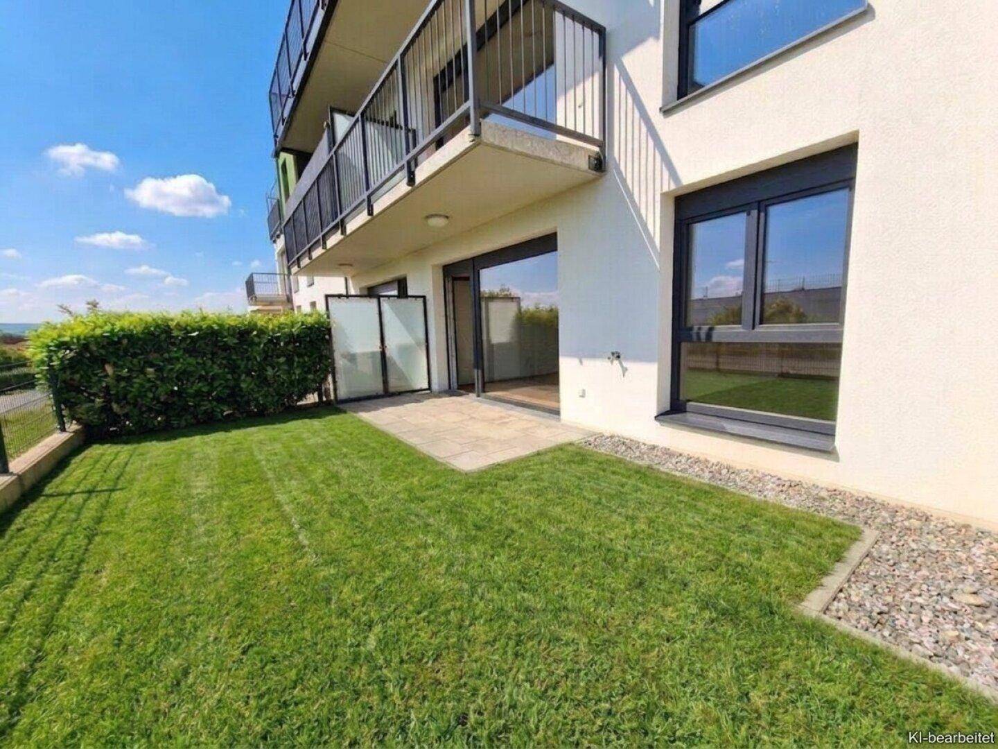 Sonniger Gartenbereich mit Rasen und Terrasse, direkt an der modernen Gebäudefassade gelegen.
