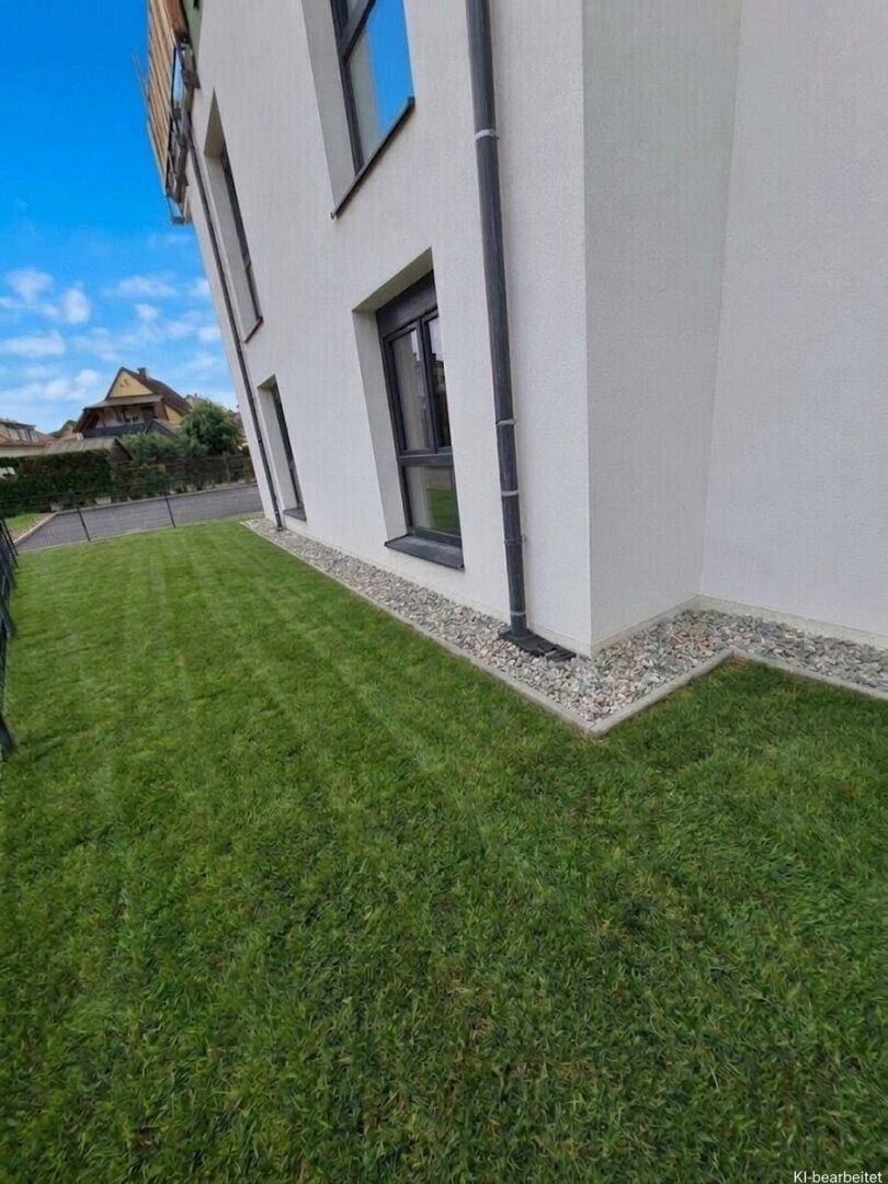 Seitenansicht eines modernen Gebäudes mit gepflegtem Rasen und einem dekorativen Kiesstreifen entlang der Fassade.