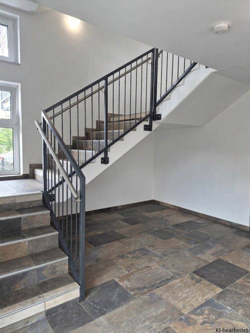 Heller Treppenaufgang mit modernem Metallgeländer und großformatigen Fliesen im Eingangsbereich des Gebäudes.