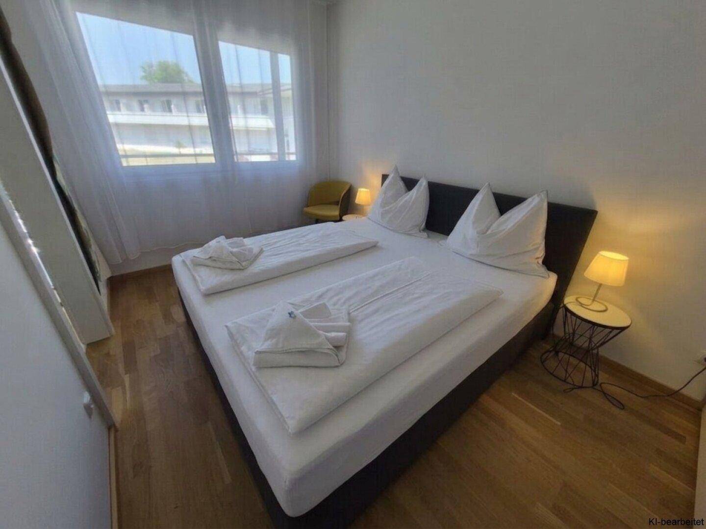 Schlafzimmer mit großem Fenster, Doppelbett und Blick auf die Außenanlage.
