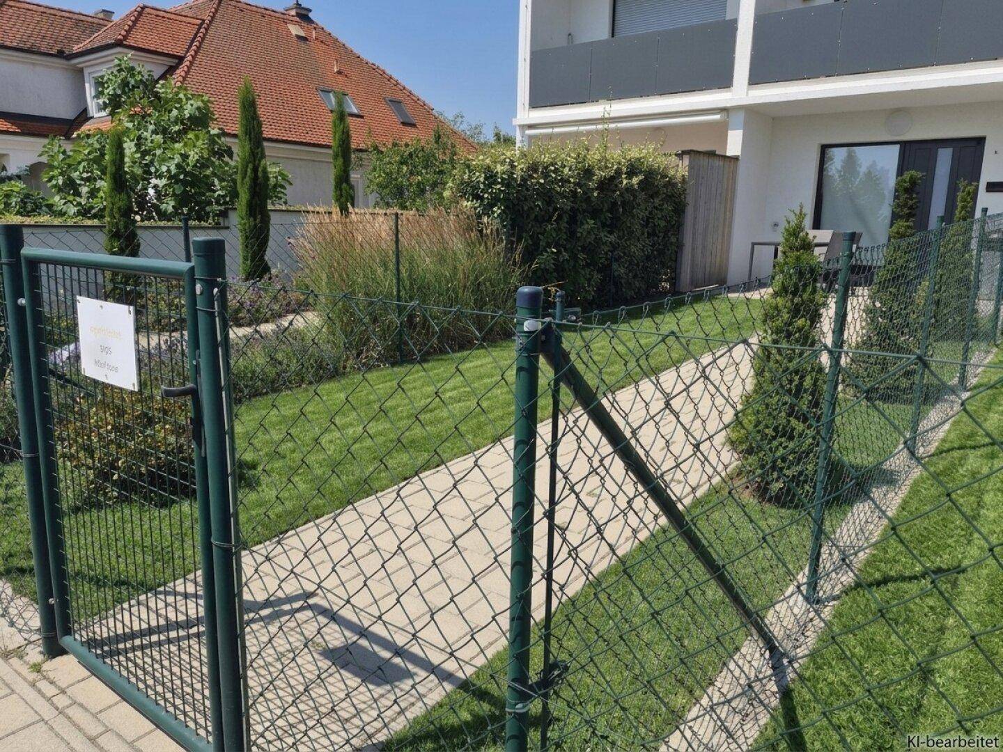 Gepflegter Gartenbereich mit Rasenfläche, Hecke und Zugang zum modernen Wohngebäude.