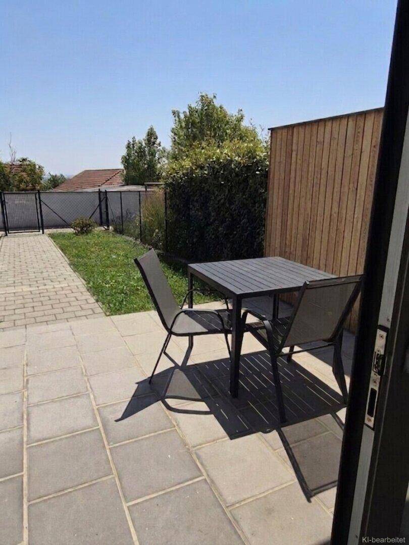 Gepflasterte Terrasse mit Gartenmöbeln und angrenzender Rasenfläche, umgeben von einer Holzwand.