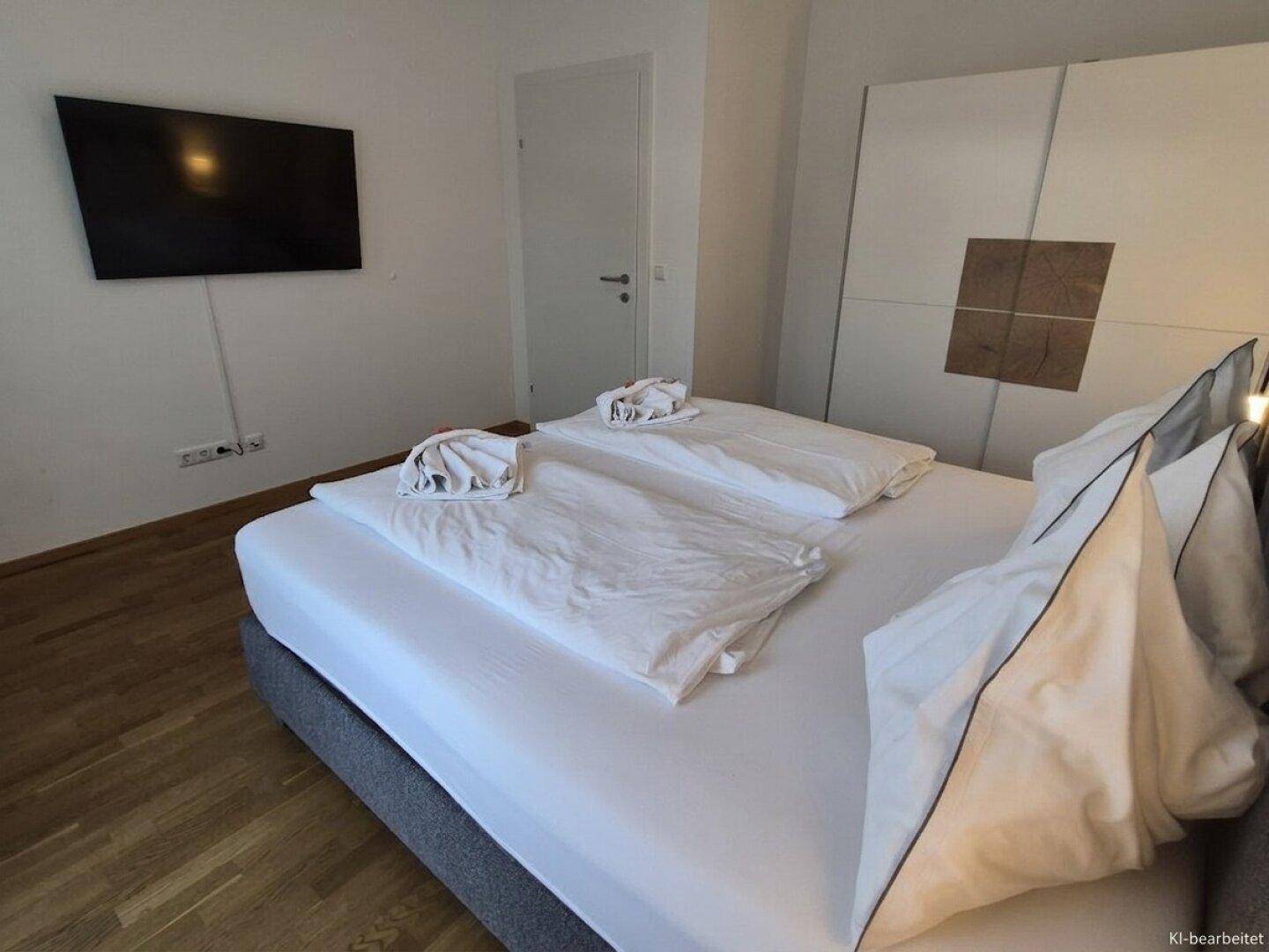 Modernes Schlafzimmer mit Holzboden, großem Bett und einem an der Wand montierten Fernseher.
