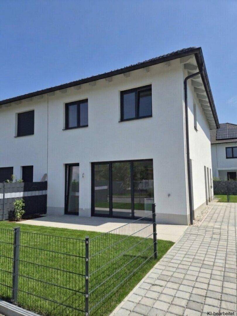 Rückseite eines modernen Hauses mit großer Glasfront und Zugang zum grünen Gartenbereich.