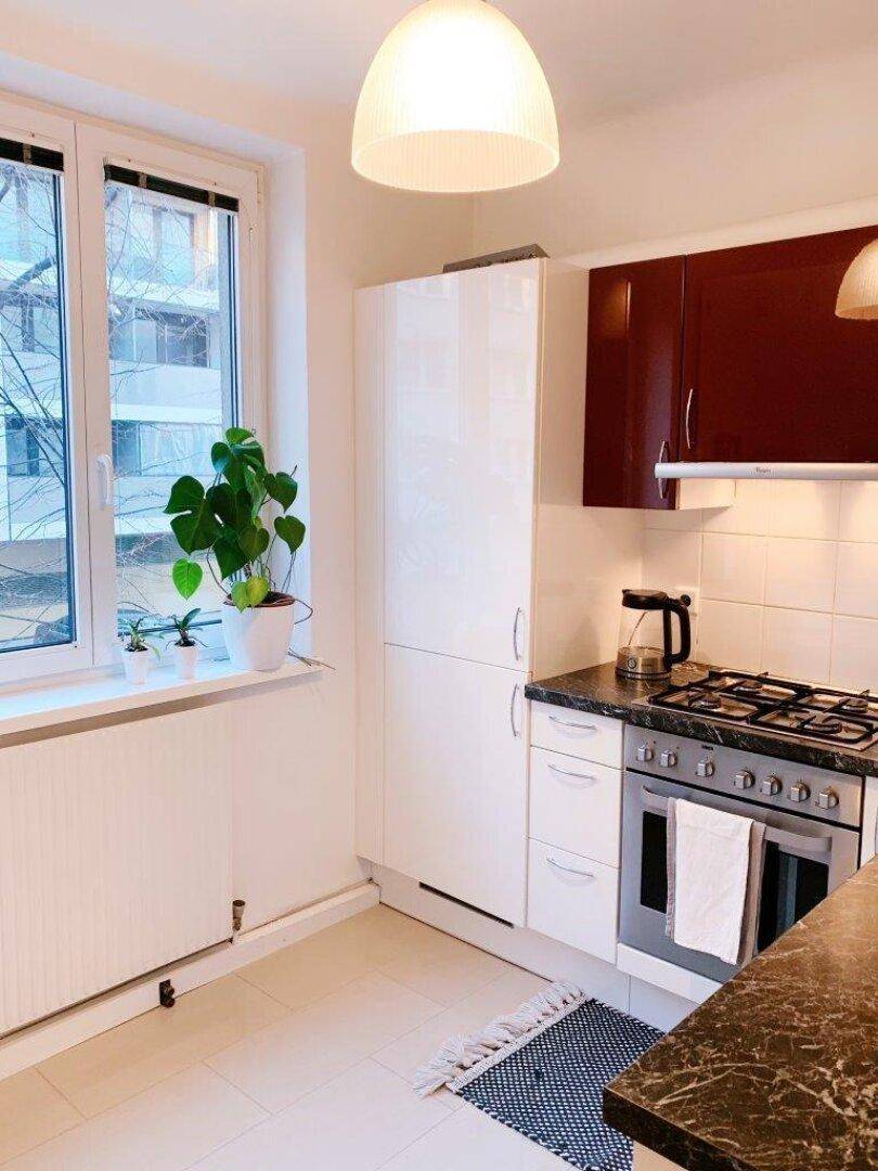 Helle Küche mit Fenster, weißen Fliesen und roten Oberschränken, bietet viel Tageslicht.