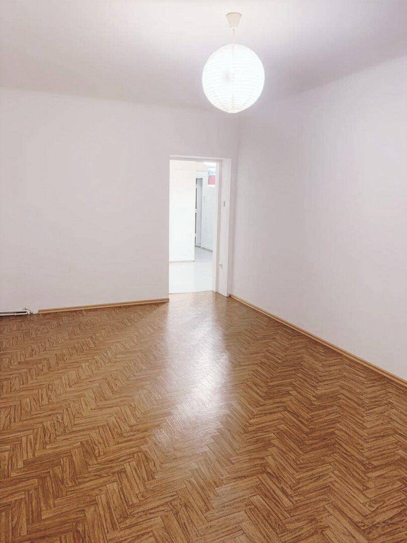 Leeres Zimmer mit Fischgrätparkett und weiß gestrichenen Wänden, bereit zur individuellen Gestaltung.